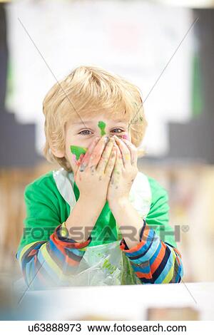 Stock Image - Boy with paint on his face and hands over mouth. Fotosearch