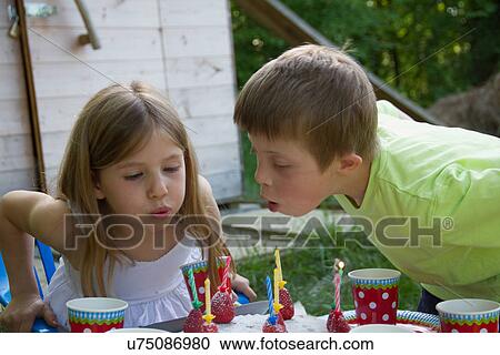 Stock Image - Brother and sister blowing out birthday candles. Fotosearch