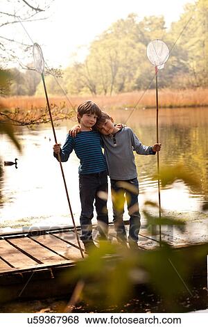 Stock Photo - Brothers standing together on pier holding fishing nets, portrait. Fotosearch