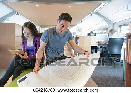 Stock Photo - Business colleagues looking at plans in modern office. Fotosearch