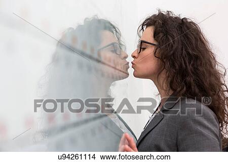 Picture - Businesswoman kissing her reflection on wall. Fotosearch