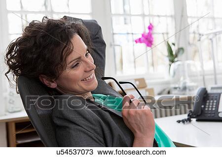 Stock Image - Businesswoman leaning back in office chair, hand in hair. Fotosearch