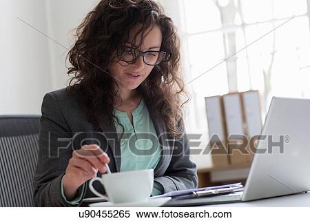 Businesswoman sitting at desk with laptop computer and coffee cup View Large Photo Image Stock Photography - Businesswoman sitting at desk with laptop computer and coffee cup. Fotosearch
