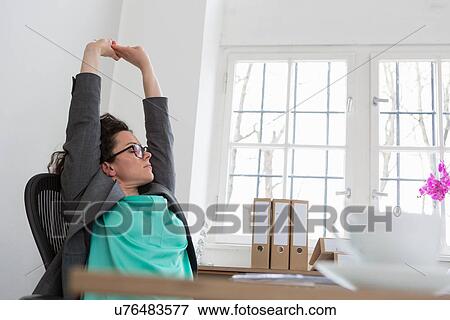 Businesswoman stretching arms up sitting in office chair View Large Photo Image Stock Photo - Businesswoman stretching arms up sitting in office chair. Fotosearch
