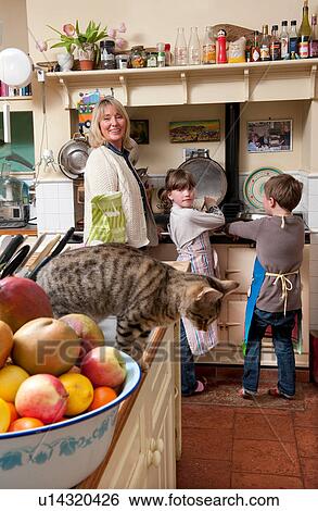 Stock Photograph - Cat looking down as mature woman, son and daughter cook in rustic kitchen. Fotosearch