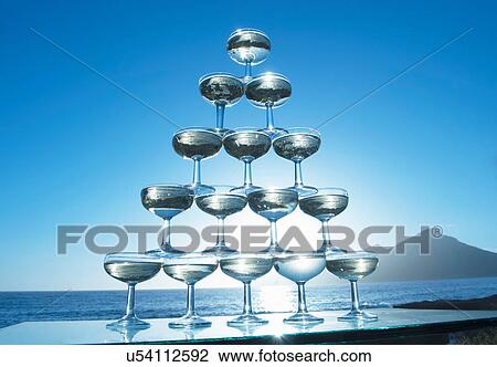 Stock Image - Champagne glasses in pyramid shape with sea in background. Fotosearch