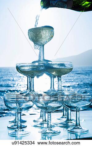 Champagne pouring into glasses with sea in background View Large Photo Image Picture - Champagne pouring into glasses with sea in background. Fotosearch