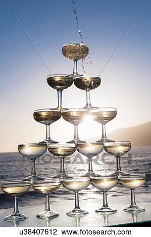Stock Image - Champagne pouring into glasses with sea in background. Fotosearch