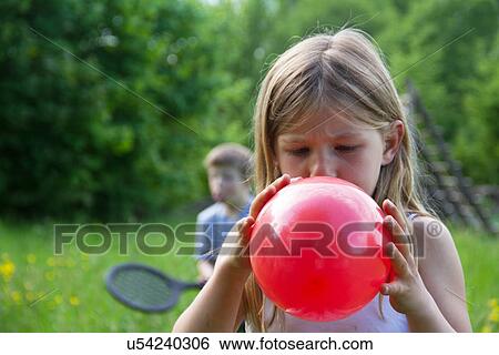 Stock Photograph - Close portrait of young girl blowing up red balloon. Fotosearch