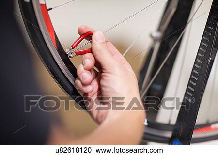 Stock Image - Close up of person using spoke wrench on bicycle wheel. Fotosearch