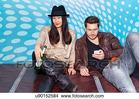 Couple sitting on floor, holding bottle of beer and smartphone View Large Photo Image Picture - Couple sitting on floor, holding bottle of beer and smartphone. Fotosearch