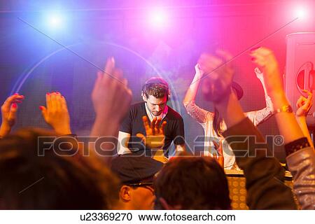 Stock Image - Disc jockey surrounded by raised arms. Fotosearch