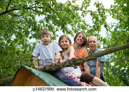 Stock Photography - Family with two children sitting on playhouse roof. Fotosearch
