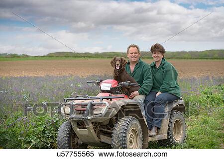 Stock Photography - Farmer, wife and pet dog on quad bike in field of organic farm. Fotosearch