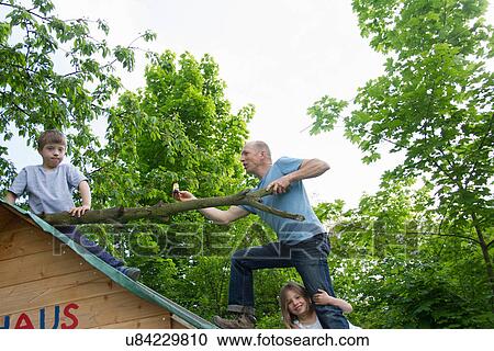 Stock Image - Father and two children climbing on playhouse roof. Fotosearch
