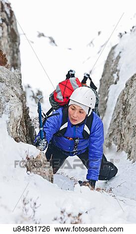 Stock Photograph - Female climber coming through snow covered ravine, Castell y Geifr, Snowdonia. Fotosearch