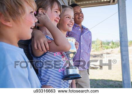 Stock Image - Four children with trophy, looking away. Fotosearch