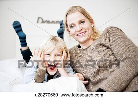 Stock Image - Fun portrait of mother and son on bed. Fotosearch