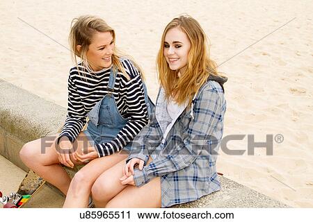 Stock Image - Girlfriends sitting on wall at beach. Fotosearch