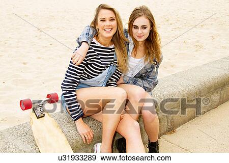 Girlfriends sitting on wall at beach with skateboard View Large Photo Image Stock Photo - Girlfriends sitting on wall at beach with skateboard. Fotosearch