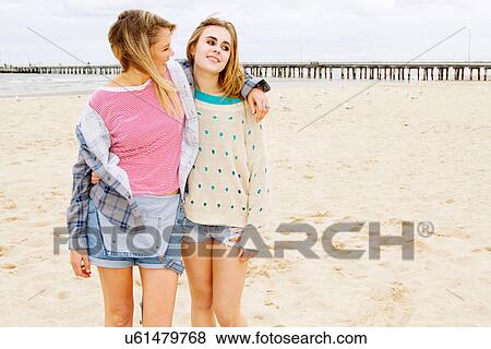 Stock Photo - Girlfriends standing on beach with arm around. Fotosearch