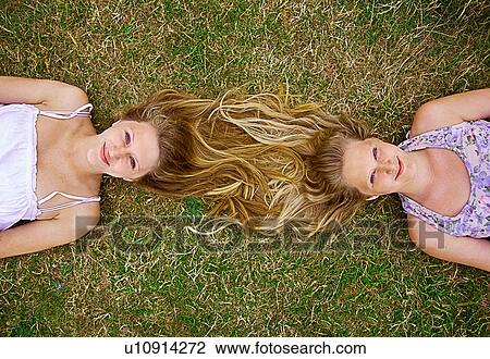 Stock Image - Girls lying in field, long hair entwined, overhead view. Fotosearch
