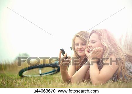 Girls lying in field, looking at smartphone View Large Photo Image Stock Image - Girls lying in field, looking at smartphone. Fotosearch