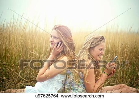 Picture - Girls using smartphones in a field, back to back. Fotosearch