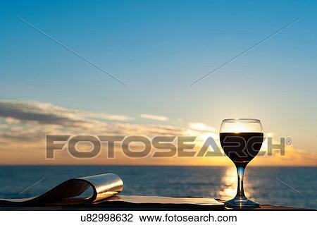 Stock Image - Glass of red wine with sea in background. Fotosearch