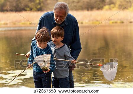 Stock Photo - Grandfather and grandsons holding fishing nets by river. Fotosearch