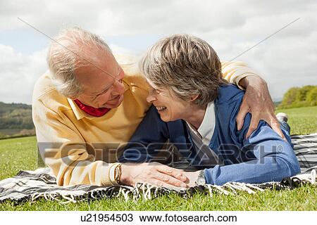Stock Image - Husband and wife lying on stomach on blanket in field. Fotosearch