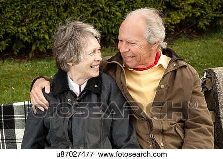 Husband and wife sharing a light moment on bench in field View Large Photo Image Stock Photo - Husband and wife sharing a light moment on bench in field. Fotosearch