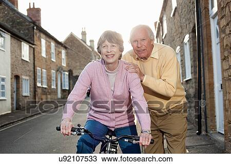 Stock Image - Husband supporting wife on bicycle. Fotosearch