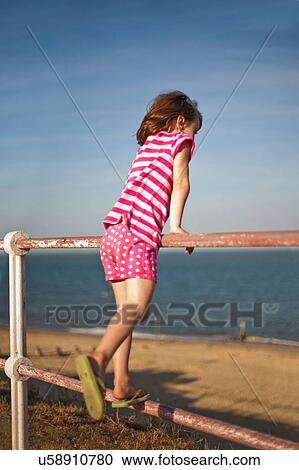 Stock Image - Little girl on railings by beach. Fotosearch