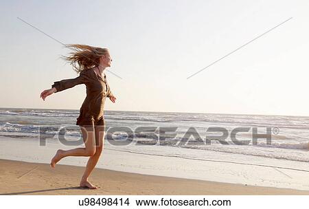 Picture - Mature woman running along beach. Fotosearch