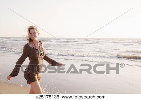 Stock Photograph - Mature woman walking along beach, smiling. Fotosearch