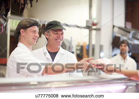 Stock Photo - Men serving customer on butcher's counter. Fotosearch