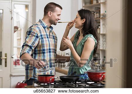 Stock Photo - Mid adult couple cooking dinner, tasting. Fotosearch