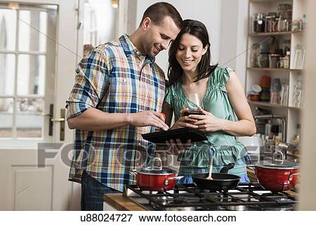 Mid adult couple cooking dinner, using digital tablet View Large Photo Image Stock Photo - Mid adult couple cooking dinner, using digital tablet. Fotosearch