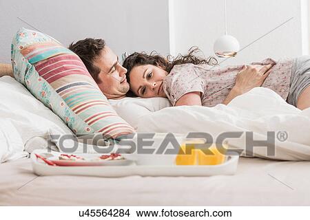 Mid adult couple lying in bed, breakfast on tray, hugging View Large Photo Image Picture - Mid adult couple lying in bed, breakfast on tray, hugging. Fotosearch