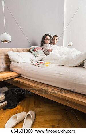 Stock Image - Mid adult couple lying in bed, breakfast on tray. Fotosearch