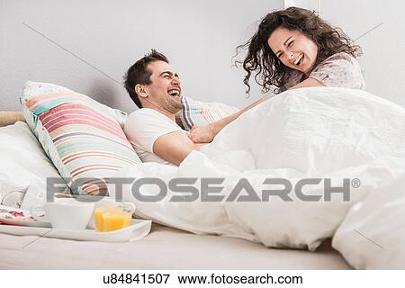 Mid adult couple lying in bed, breakfast on tray, pillow fight View Large Photo Image Stock Photo - Mid adult couple lying in bed, breakfast on tray, pillow fight. Fotosearch