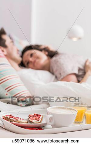 Mid adult couple lying in bed, breakfast on tray, hugging View Large Photo Image Stock Photograph - Mid adult couple lying in bed, breakfast on tray, hugging. Fotosearch