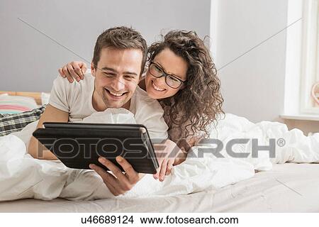 Mid adult couple lying on bed using digital tablet View Large Photo Image Picture - Mid adult couple lying on bed using digital tablet. Fotosearch