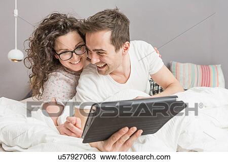 Mid adult couple lying on bed using digital tablet View Large Photo Image Stock Image - Mid adult couple lying on bed using digital tablet. Fotosearch