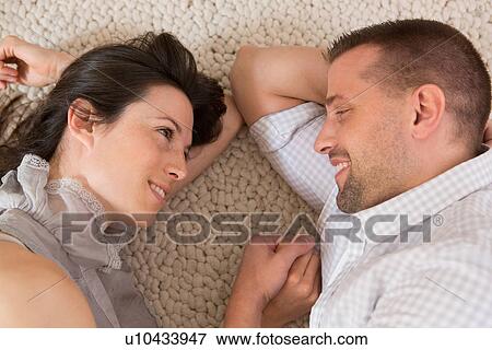 Stock Photo - Mid adult couple lying on floor face to face. Fotosearch