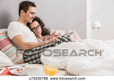 Mid adult couple reading newspaper in bed View Large Photo Image Stock Photo - Mid adult couple reading newspaper in bed. Fotosearch
