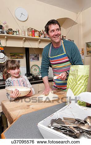Stock Photograph - Mid adult man and daughter baking in rustic kitchen. Fotosearch