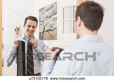 Stock Photo - Mid adult man holding up ties against shirt. Fotosearch