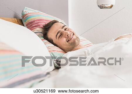 Stock Photo - Mid adult man lying in bed under duvet. Fotosearch